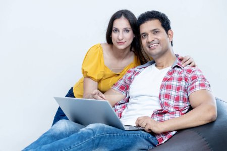 Photo for Young indian latin couple with laptop sitting on bean bag looking towards the camera , Family lifestyle concept - Royalty Free Image