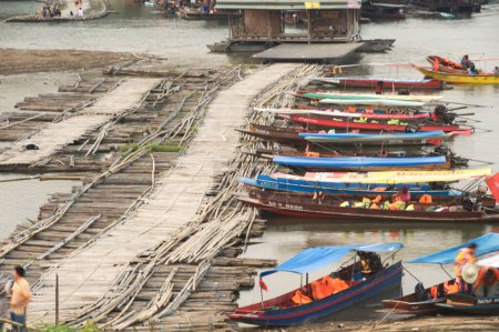Téléchargez les photos : KANCHANABURI, THAÏLANDE - 16 AVRIL 2016 : Un groupe non identifié de bateaux à longue queue emmène les touristes le long de la rivière Songkhalia près du pont Mon ou du pont Uttamanusorn. Situé Amphoe Sangkhlaburi, Kanchanaburi Province, Thaïlande. - en image libre de droit