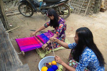 MINDAT, MYANMAR - 6 DE DICIEMBRE DE 2018 Una mujer no identificada de la tribu de la Luna, Mindat, estado de Chin, teje tela sobre un telar tradicional en el patio de una casa.