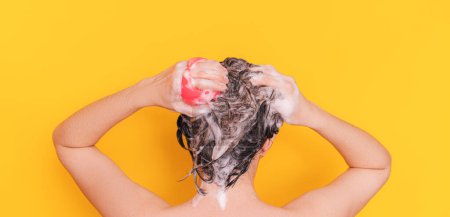 Téléchargez les photos : Lady with foam in her hair takes care of her scalp with pink color massager against yellow background. - en image libre de droit