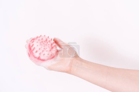 Scalp massager in hand and in foam against white background.