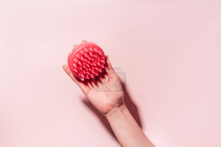 Téléchargez les photos : Masseur du cuir chevelu rose à la main féminine sous une lumière dure sur fond rose. - en image libre de droit