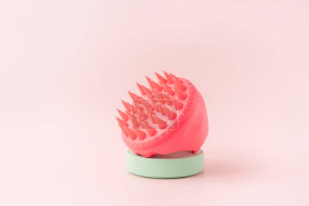 Téléchargez les photos : Pink color scalp massager on green stand against pink background. - en image libre de droit