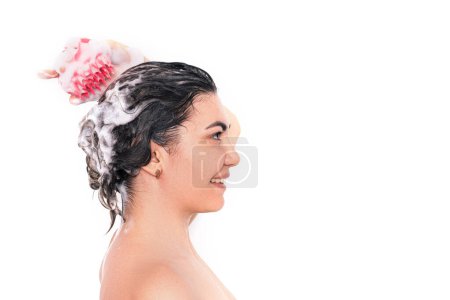 Lady with soapy head takes care of the scalp with massager in pink against white background.