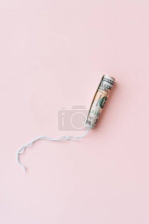 Téléchargez les photos : Tampon enveloppé dans un billet de cent dollars sur fond rose. - en image libre de droit
