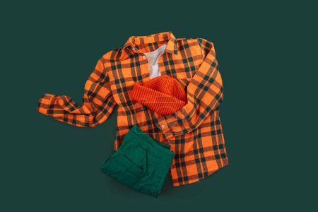Photo for Childrens clothing set with a plaid shirt, an orange hat and green pants on a green background. - Royalty Free Image