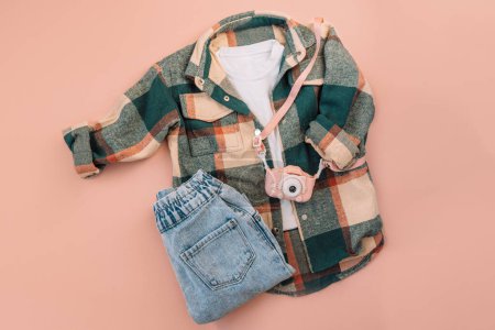 Photo for Childrens checkered shirt and blue jeans with digital camera on pink background. - Royalty Free Image