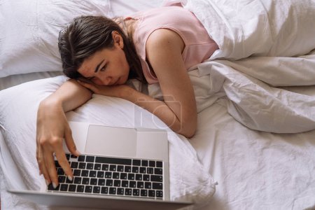 Lady working remotely while lying in bed with laptop.