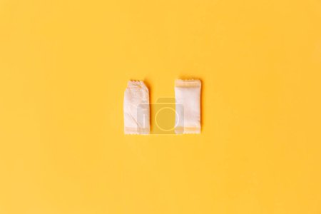 Two white snus bags, one used and the other new on a yellow background.