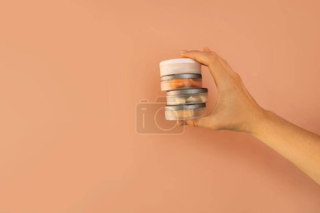 Hand holding plastic jars filled with snus against brown background.