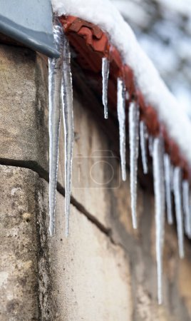 Téléchargez les photos : Gros plan sur des stalactites de glace formées sur le bord supérieur d'un mur. - en image libre de droit