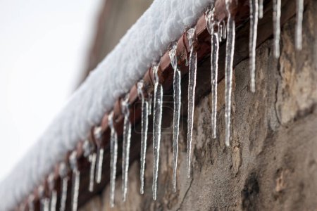 Close-up on ice stalactites formed at the top edge of a wall.