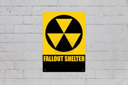 Photo for Yellow warning sign screwed to a brick wall to warn about a threat. In the middle of the panel, there is a nuclear symbol and the message is saying "Fallout shelter". - Royalty Free Image