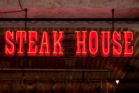 Téléchargez les photos : Lumière au néon rouge en forme de mots "Steak house" au-dessus de la vitrine d'un restaurant. - en image libre de droit