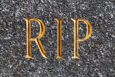 Close-up on the acronym "RIP" (Rest In Peace) engraved in gilded in a granite tombstone.