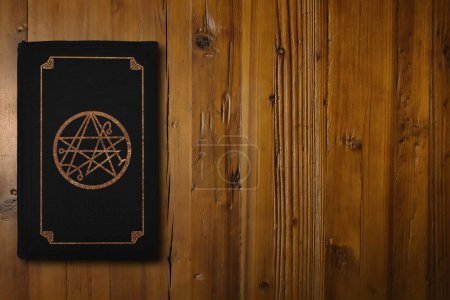 Photo for Close-up on a black book with a the gilded sigil of the gateway on a brown woodboard. - Royalty Free Image