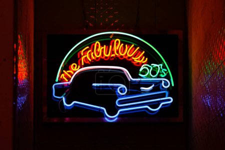 Téléchargez les photos : Lumière au néon sur un mur de briques disant "Les fabuleuses années 50" au-dessus d'une voiture rétro. - en image libre de droit