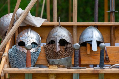 Helmets, swords and other weapons of war from the medieval period stored on a wooden rack.