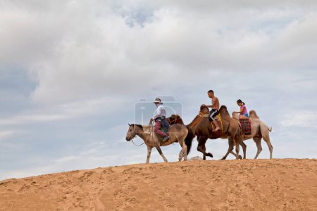 Foto de Elsen Tasarkhai, Mongolia - 04 de agosto de 2018: Tres turistas en una duna de "Mini Gobi", uno montado en un caballo y los otros dos en un camello bactriano. - Imagen libre de derechos