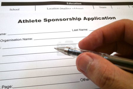 Foto de Una pluma sostenida por un dedo de alguien listo para llenar un formulario de solicitud de patrocinio de atleta. - Imagen libre de derechos