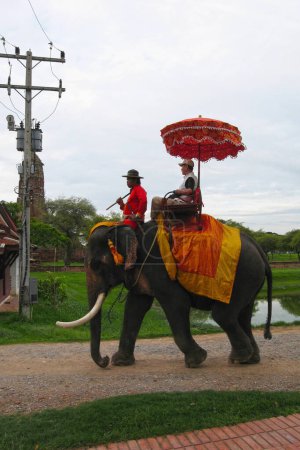 Téléchargez les photos : Ayutthaya, Thaïlande - 30 juin 2006 : Mahout vêtu de vêtements traditionnels chevauchant un éléphant avec un touriste asiatique derrière lui autour des monuments d'Ayutthaya, Thaïlande. - en image libre de droit
