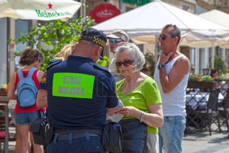 Photo for Krakow, Poland - June 06 2019: Municipal police officers (Straz Miejska) helping out an old tourist lady at the main market square in the Old Town. - Royalty Free Image
