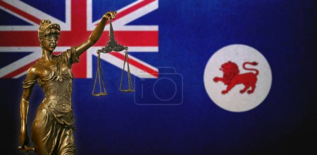 Nahaufnahme einer kleinen Bronzestatuette der Lady Justice vor einer Flagge Tasmaniens (Australien)).
