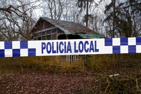 Abandoned cabin in the woods with a police tape with written in it in Spanish "Policia local".