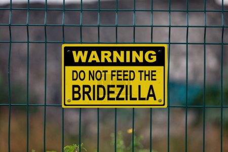 Warning sign on a fence stating in "Warning, do not feed the Bridezilla"