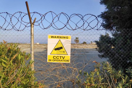 Panneau attaché à la clôture d'une friche industrielle au bord de la mer indiquant : Avertissement, CCTV en service.