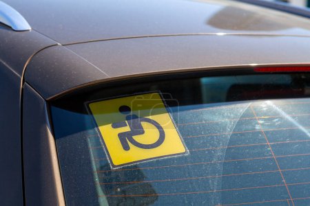 Close-up on a yellow "disabled driver" sign stuck at the rear window of a car.