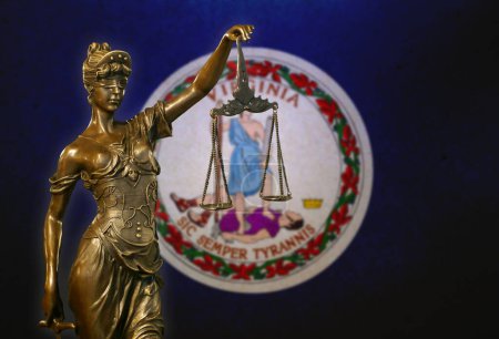 Nahaufnahme einer kleinen Bronzestatuette der Lady Justice vor einer Flagge von Virginia.