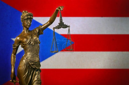 Nahaufnahme einer kleinen Bronzestatuette der Lady Justice vor einer Flagge Puerto Ricos.