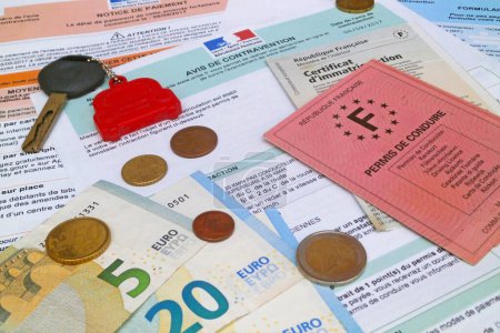 A French driver's license, a vehicle registration certificate, a car key and some euro coins and banknotes on the top of a french speeding ticket with the details of the infraction and the date. All identifications have been cleaned up.