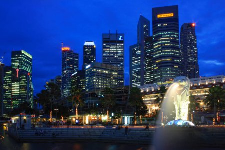 Photo for Singapore, Singapore - August 22 2007: Tourists seated on the stairs enjoying the view from Merlion Park at dusk. Behind the Merlion is the Central Business District. - Royalty Free Image