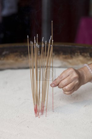 Woman adding an encent stick to an encent burner in the Tooth Relic Pagoda In Singapore.