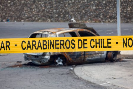 Téléchargez les photos : Voiture brûlée par un pyromane avec une bande de police avec écrit en espagnol "Carabineros de Chile - No pasar". - en image libre de droit