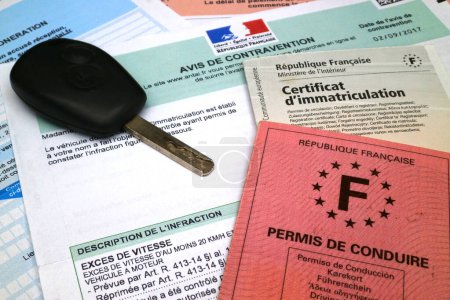 Ein französischer Führerschein, ein Fahrzeugschein und ein Autoschlüssel auf der Oberseite eines französischen Geschwindigkeitsscheines mit den Details des Verstoßes und dem Datum. Alle Identitäten wurden bereinigt.