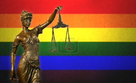 Close-up of a small bronze statuette of Lady Justice before the Rainbow flag.