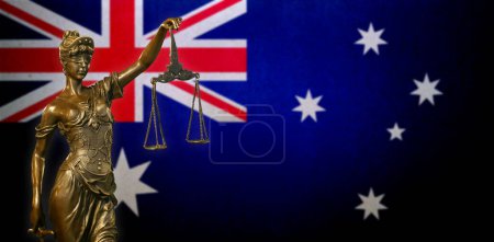 Nahaufnahme einer kleinen Bronzestatuette der Lady Justice vor einer australischen Flagge.