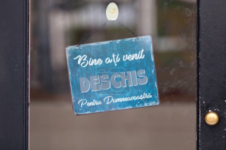 Panneau bleu ouvert avec écrit en roumain : "Bine ati venit ! DESCHIS Pentru Dumneavoastra. ", signifiant en anglais" Bienvenue ! OUVERT Pour vous.".
