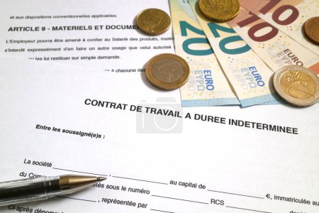 A ballpoint pen and some euro coins and banknotes on the top of a French Employment contract of indefinite duration (Contrat de travail  duree indeterminee).