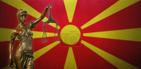 Nahaufnahme einer kleinen Bronzestatuette der Frau Gerechtigkeit vor einer Flagge Nordmakedoniens.