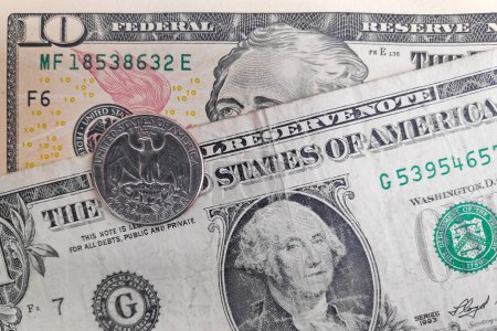 Primer plano de una moneda de un cuarto de dólar encima de un billete de 1 y 10.