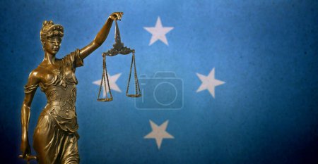 Nahaufnahme einer kleinen Bronzestatuette der Lady Justice vor einer Flagge der Föderierten Staaten von Mikronesien.