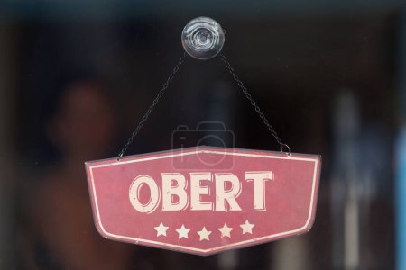 Panneau à l'ancienne dans la fenêtre d'un magasin disant en catalan "Obert", signifiant en anglais "Ouvert".