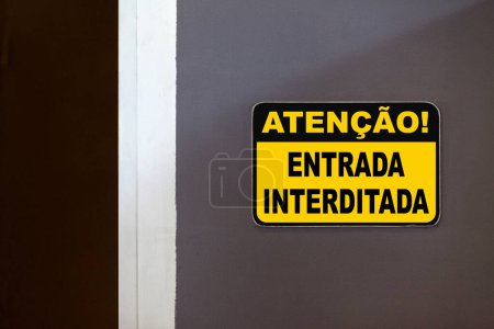 Yellow and black warning sign on the side of an open door stating in Portuguese "Atencao - Entrada interditada", meaning en English "Attention - Restricted entry".