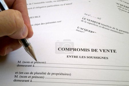 A ballpoint pen between the fingers of a man filling a French property sales agreement.