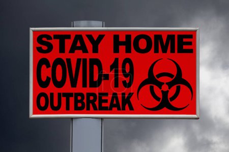 Close-up on a red billboard against a stormy sky with the message "Stay home, COVID-19 outbreak" written in the middle.