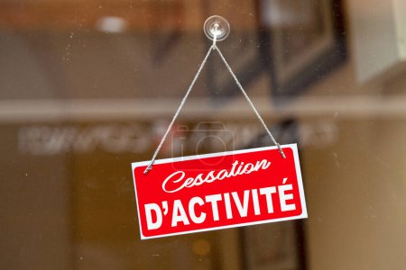 Red sign anging at the glass door of a shop saying in French: "Cessation d'activite" meaning in English "Cessation of activity".